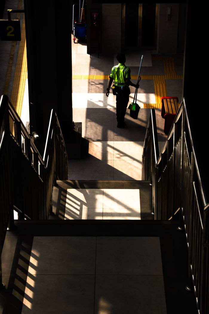 Silhouette of a worker cleaning in a sunlit metro station.
